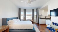 Located at 1659 Ocean Front Walk in Santa Monica, California, this efficiently designed studio offers a well-organized layout that maximizes every square foot. Rich hardwood flooring flows throughout the space, lending warmth and continuity to the open floor plan.

The main living and sleeping area is the heart of the studio, featuring large, multi-pane windows dressed with bold black-and-white striped curtains that frame views of surrounding palm trees and the sunny California sky. A ceiling fan overhead ensures comfortable airflow, while wall-mounted sconce lighting adds a refined touch to the ambiance.

The galley-style kitchen is thoughtfully appointed with crisp white cabinetry, black hardware, dark countertops, and stainless steel appliances including a full-size range, refrigerator, and microwave. A matte black faucet over the sink and a tile backsplash add modern detailing throughout.

The interior decor maintains a clean, coastal aesthetic with white walls, tropical greenery, and beach-inspired artwork, creating a bright and airy atmosphere. The entry area features a smart lock door, wall art, and a decorative pendant light, rounding out a cohesive and stylish space ideally situated steps from the iconic Santa Monica beachfront.