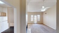 Located at 2900 W Highland St in Chandler, Arizona, this single-floor residence offers a well-organized layout with comfortable living spaces throughout. The living room is generously sized, featuring plush carpeting, a textured ceiling, a ceiling fan with light fixture, and French doors that open to an outdoor area, allowing natural light to flow in. An adjoining dining area is illuminated by a pendant light and flanked by multiple windows that bring in additional sunlight and views of the surrounding neighborhood. The kitchen is efficiently designed in a U-shaped configuration, equipped with light wood cabinetry, dark speckled countertops, a double-basin sink, white appliances including a range, dishwasher, and over-the-range microwave, plus tile flooring and a window above the sink. The bedrooms are carpeted and include ceiling fans, ample windows with vertical blinds, and closet access. One bedroom features a door with sidelight leading to an exterior space. The bathrooms are clean and functional — one includes a shower/tub combo with white tile surround and grab bars, while another features a wide vanity with dual sinks, a full-width mirror, and dark speckled countertops matching the kitchen. The home maintains a neutral, warm color palette throughout, creating a cohesive and inviting atmosphere.