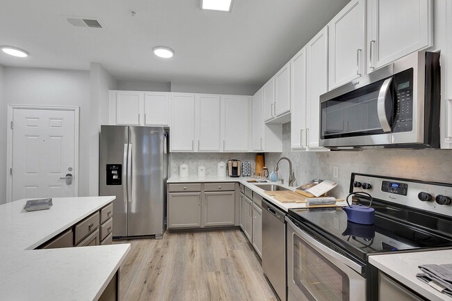 Modern kitchen with sleek stainless steel appliances, elegant white cabinetry, and stylish wood flooring, perfect for culinary enthusiasts. - Avia Lowry