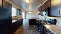 This two-story home offers a practical and well-appointed layout across both levels. The main floor centers around an open-concept living, dining, and kitchen area. The kitchen is generously sized, featuring rich dark-wood cabinetry, laminate countertops, a kitchen island, and black appliances including a range, microwave, and refrigerator, all set atop durable wood-look flooring. The dining area is illuminated by an elegant chandelier and opens directly to the outdoors through a sliding glass door, allowing natural light to flow throughout. The living room transitions seamlessly from the dining space, with plush carpeting adding warmth and comfort. A staircase connects the main floor to the upper level. Also on the main floor is a convenient half bathroom and a dedicated laundry area equipped with a full-size washer and dryer beneath an overhead storage shelf. Upstairs, the bedrooms feature soft carpeting, neutral wall tones, and windows with blinds that provide natural light and privacy. The vaulted ceiling in one of the upper bedrooms adds architectural interest and a sense of openness. A full bathroom upstairs includes a single-sink vanity with dark wood cabinetry, a tub-shower combination, and tile flooring, completing this functional and comfortable home.