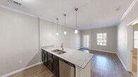 Located in Austin, TX (78754), this well-appointed 1-bedroom, 1-bathroom home offers a thoughtfully designed single-floor layout. The open-concept kitchen and living area serves as the heart of the home, featuring dark espresso cabinetry, granite countertops, a subway tile backsplash, and a full suite of stainless steel appliances including a refrigerator, electric range, and microwave. A peninsula with a double-basin sink and pendant lighting overhead creates a natural divide between the kitchen and the adjacent dining area, which is highlighted by a modern multi-bulb chandelier. The living room benefits from wood-look flooring, crown molding, and a glass door flanked by windows that invite natural light and outdoor views. The spacious bedroom offers plush carpeting, a ceiling fan, and a window with exterior views, while a dedicated closet provides ample storage. The hallway connects the private and common areas with ease. The bathroom includes a tub/shower combo with white subway tile surround and tile flooring. Throughout, neutral gray walls, white trim, and consistent finishes create a clean, cohesive aesthetic suited for comfortable everyday living.