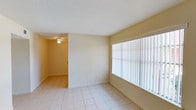 This single-floor, 2-bedroom, 1-bathroom unit offers a straightforward and functional layout designed to maximize everyday comfort. Light-toned ceramic tile flooring runs consistently throughout the entire unit, creating a cohesive and easy-to-maintain interior. The living area features a large window fitted with vertical blinds, allowing ample natural light to fill the space, while an adjacent section connects seamlessly to the rest of the unit via an open passageway. A second living or dining area also benefits from a large picture window that looks out onto greenery, providing pleasant outdoor views and additional natural light. Each bedroom is equipped with a ceiling fan with integrated lighting and features windows with horizontal blinds for light control. The primary bedroom includes two closets with bi-fold doors, offering generous storage capacity. The second bedroom mirrors the same functional design with its own ceiling fan and window. The bathroom is well-appointed with tile-surround tub and shower combo, a toilet, and a vanity with a sink. Textured ceilings are featured in select areas of the unit, adding a subtle design detail. Overall, the unit presents a clean, neutral palette that provides a versatile canvas for personalization.