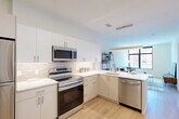 Located at 2 West 4th Street in downtown Wilmington, Delaware, this thoughtfully designed one-bedroom, one-bathroom unit offers a clean, modern aesthetic throughout its well-utilized single-floor layout. Light oak-toned flooring flows seamlessly from room to room, complementing the bright white walls and creating a cohesive, contemporary feel.

The kitchen is a standout feature, outfitted with crisp white cabinetry extending to the ceiling, white quartz countertops, a subway tile backsplash, and a full suite of stainless steel appliances including a refrigerator, electric range, over-the-range microwave, and dishwasher. Pendant lighting and an open sightline to the living area enhance both function and style.

The living room benefits from large, black-framed windows that frame views of the surrounding streetscape, flooding the space with natural light and creating an airy urban atmosphere.

The bedroom is a comfortable retreat with light-filled walls and direct access to a dedicated closet. The bathroom features a tub-shower combination with clean white tile surround, a vanity with storage, and consistent warm-toned flooring.

A dedicated in-unit laundry area houses a full-sized washer and dryer — a practical and convenient addition. The unit's modern finishes, efficient layout, and central Wilmington location make it a compelling urban residence.
