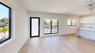 Located at 100 SW 14th St in Boca Raton, FL, this single-story 3-bedroom, 2-bathroom unit offers a clean, modern aesthetic throughout. Light wood-tone flooring flows seamlessly across every room, complementing the bright white walls and creating a cohesive, airy atmosphere. The open-concept living room is filled with natural light from large black-framed windows and a glass door that frame outdoor views of the surrounding neighborhood's lush greenery.

The kitchen is a standout feature, equipped with high-gloss white cabinetry extending to the ceiling, stainless steel appliances including a range, microwave, and refrigerator, and a generous white waterfall island that doubles as additional workspace and seating. Recessed lighting adds a polished touch overhead.

The primary bedroom is a spacious retreat, while the two additional bedrooms each offer ample room, closet storage, and windows that bring in plenty of natural light. All bedrooms continue the light flooring found throughout the unit.

Both bathrooms are finished with striking floor-to-ceiling marble-patterned tile in the walk-in showers, paired with crisp white fixtures and wood-look flooring for a refined, contemporary feel. Two hallways connect the living spaces efficiently, contributing to the unit's well-organized layout.