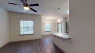 Located at 300 E Swisher Rd in Lake Dallas, Texas, this single-story residence offers a well-designed, open-concept floor plan that seamlessly connects the main living areas. The living room is bright and welcoming, featuring rich hardwood-style flooring, a ceiling fan with light fixture, and multiple windows dressed with horizontal blinds that allow ample natural light to filter in. It flows naturally into the dining area, which is illuminated by a stylish pendant light, reinforcing the cohesive open layout.

The kitchen is a standout feature, equipped with dark cabinetry, black appliances including a range, microwave, and refrigerator, and a granite-topped peninsula island with an integrated sink and pendant lighting above. The island provides additional counter space and serves as a practical divider between the kitchen and living areas.

The bedrooms are carpeted for comfort, each outfitted with a ceiling fan. The primary bedroom includes access to a walk-in closet with built-in shelving, offering generous storage. The bathroom features dark cabinetry with a wide vanity, a large mirror, and hardwood-style flooring that ties back to the main living areas.

Throughout, the neutral color palette of warm whites and greiges creates a clean, move-in-ready atmosphere suited for everyday living.