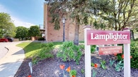 This single-floor space is situated within a distinguished brick building that exudes a timeless, professional character. The exterior showcases classic brick masonry with arched architectural detailing, complemented by a multi-story structure that speaks to the building's substantial presence. The surrounding grounds are thoughtfully landscaped, featuring mature evergreen and deciduous trees that provide natural shade and a sense of established permanence. Seasonal plantings, including vibrant red tulips and well-maintained shrub beds with fresh mulch, add color and curb appeal to the property. A traditional lamp post anchors the entryway area, contributing to the welcoming and polished ambiance of the exterior. A prominently placed property sign near the entrance identifies the building and provides contact information, suggesting a professional or commercial use. The grounds are neatly kept, with manicured greenery lining the walkways and building perimeter. An upper-level balcony is also visible on the structure, hinting at additional amenity spaces above. Overall, the property presents a clean, organized, and inviting atmosphere supported by its well-maintained brick facade and carefully curated landscaping.