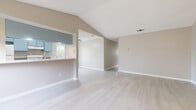 This single-story, 3-bedroom, 3-bathroom home offers a thoughtfully designed layout with a clean, neutral aesthetic throughout. The open living area immediately impresses with its dramatic vaulted ceilings that amplify the sense of space, complemented by light wood-style flooring that runs seamlessly across the entire floor. Natural light filters in through multiple windows, creating a bright and welcoming atmosphere.

The kitchen features a galley-style design with distinctive blue cabinetry, granite-look countertops, a gas range, and ample upper and lower cabinet storage. A window above the sink provides a pleasant outdoor view of surrounding greenery. The kitchen connects to the living area via a convenient pass-through counter.

Each of the three bedrooms is well-proportioned, with ceiling fans, large windows with natural views, and light flooring. Each bedroom is paired with its own closet, offering practical storage solutions. The primary bedroom provides a comfortable, private retreat.

The three bathrooms maintain the home's cohesive style, featuring blue vanity cabinetry with granite countertops and large mirrors. Additional bathrooms include tub-shower combinations with clean, white fixtures. Neutral warm-gray wall tones are consistent throughout, tying the entire home together into a cohesive and functional living space.