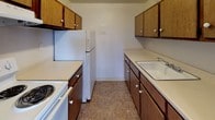 This single-floor, two-bedroom, one-bathroom unit in Ypsilanti, MI offers a straightforward and functional layout. The living room is the largest space in the unit, featuring wall-to-wall carpeting, neutral white walls, and a sliding glass door that opens to a private balcony overlooking outdoor greenery, allowing natural light to fill the room. Adjacent to the living area, the galley-style kitchen is equipped with dark wood cabinetry along both walls, white appliances including a range and refrigerator, light countertops, a single-basin sink, and durable vinyl tile flooring.

Both bedrooms are carpeted and finished with the same neutral tones as the rest of the unit. Each room includes at least one sliding or standard window that brings in natural light and provides views of the surrounding neighborhood. The single full bathroom features a white tile surround tub-shower combination, a vanity with sink, and vinyl tile flooring, maintaining a clean and functional aesthetic throughout. The overall layout, as seen in the floor plan, provides a logical flow between the living, dining, and kitchen areas, with the bedrooms positioned for privacy.