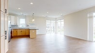 This well-designed single-floor residence offers a clean, contemporary aesthetic highlighted by light-toned luxury vinyl plank flooring and neutral wall finishes throughout the main living areas. The open-concept kitchen and living space serves as the heart of the home, featuring warm wood cabinetry, dark countertops, stainless steel appliances including a refrigerator, range, and microwave, and a central island with pendant lighting overhead. Large floor-to-ceiling windows and a sliding glass door in the living area flood the space with natural light and provide views of the surrounding neighborhood. A dedicated hallway connects the main living space to the private areas of the home, which include multiple carpeted bedrooms, each benefiting from their own windows that invite additional natural light. The bathroom is finished with a clean white vanity countertop, light wood cabinetry, and a mirror above the sink. A dedicated laundry room houses a full-sized Whirlpool washer and dryer set with wire shelving above for additional storage. The overall ambiance of the space is bright, clean, and move-in ready, with a consistent modern design language carried throughout every room.