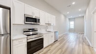 This thoughtfully designed single-floor unit offers a clean, contemporary aesthetic throughout. The kitchen is a standout feature, showcasing crisp white shaker cabinetry, white subway tile backsplash, and light quartz countertops. A full suite of stainless steel appliances — including a refrigerator, electric range, over-the-range microwave, and dishwasher — provides everything needed for modern cooking. Light-toned hardwood flooring runs seamlessly throughout the space, enhancing the bright and airy atmosphere created by recessed lighting and neutral wall tones.

The bedroom areas are generously proportioned, featuring tall ceilings and built-in closets with shelving for ample storage. One bedroom benefits from a trio of large windows that frame open urban views, flooding the room with natural light.

The bathroom is elegantly finished with floor-to-ceiling marble-look tile, extending across both the walls and flooring. A soaking tub with an overhead shower and built-in niche shelving completes the refined, spa-like feel of this room.

The open floor plan, visible in the dollhouse view, highlights a well-connected layout with clear sightlines between the kitchen and living areas. The overall design is modern, clean, and move-in ready, with high-quality finishes that reflect a commitment to both style and functionality.