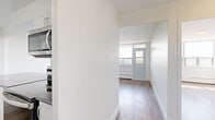 Located at 3390 Keele Street, Unit 514 in Toronto, this one-bedroom, one-bathroom unit offers a well-planned layout across a single floor. Light-toned hardwood flooring runs throughout, lending warmth and continuity to the space.

The combined kitchen and living area forms the heart of the unit. The kitchen is outfitted with white cabinetry, a classic subway tile backsplash, dark countertops, and a full suite of stainless steel appliances including a refrigerator, stove, microwave, and dishwasher. A central island provides additional counter space and separates the kitchen from the living area. The living room is particularly notable for its expansive floor-to-ceiling windows, which flood the space with natural light and offer open views of the surrounding Toronto cityscape and greenery.

The bedroom is a comfortable size, featuring mirrored sliding closet doors that enhance the sense of space, along with access to the bathroom. The bathroom is finished with crisp white subway tile surrounding the bathtub and shower, maintaining the clean, modern aesthetic found throughout the unit.

A hallway connects the main living areas and provides practical circulation throughout. The overall design is clean, bright, and contemporary, making efficient use of every area.