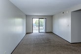 This single-floor residence offers a practical and comfortable layout designed for everyday living. The spacious living room is finished with wall-to-wall carpet, neutral-toned walls, and a textured ceiling. A ceiling fan with a light fixture provides overhead illumination, while a sliding glass door opens directly onto a private balcony, allowing natural light to fill the room and offering views of the surrounding greenery and outdoor surroundings. The layout flows conveniently from the living area toward the kitchen, which features white cabinetry with ample upper and lower storage, a coil-top range, a dishwasher, and a range hood — all set against neutral countertops and easy-to-maintain flooring. The bedrooms are carpeted and well-sized, each with neutral walls and windows fitted with blinds that allow for controlled natural light. One bedroom features a notably large window overlooking outdoor greenery, creating a bright and pleasant atmosphere. The bathroom includes a wide vanity countertop with an undermount sink, white cabinetry beneath for storage, and a large mirror with a built-in medicine cabinet. Throughout the space, dark wood baseboards and door frames provide a consistent design detail, contributing to a cohesive and understated aesthetic.