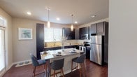 This single-story, one-bedroom, one-bathroom residence offers a thoughtfully designed layout with modern finishes throughout. The kitchen serves as a central highlight, featuring dark espresso cabinetry that extends to the ceiling for generous storage, granite countertops, and a full suite of stainless steel appliances including a refrigerator, dishwasher, and range. A substantial kitchen island with a granite surface provides seating for multiple guests and doubles as a casual dining area, illuminated by sleek pendant lighting overhead. Rich wood-style flooring flows consistently through the main living areas, adding warmth and cohesion.

The living room is bright and welcoming, with multiple windows dressed in blinds that allow natural light to filter in, complemented by a ceiling fan for comfort. The bedroom features a bold accent wall, a ceiling fan, natural light from a window, and direct access to a dedicated walk-in closet with built-in shelving. The bathroom includes a full soaking tub and shower combination with tile surround, a dark vanity with granite countertops, and wood-style flooring that ties back to the rest of the unit. Overall, the space presents a cohesive, contemporary aesthetic with functional, quality finishes throughout.