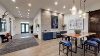 The Marq's single-floor clubhouse showcases a refined modern farmhouse design that seamlessly integrates rustic and contemporary elements. Throughout the space, white shiplap walls contrast with warm wood-look flooring, creating a cohesive and inviting aesthetic. The entry area features a welcoming foyer with large glass double doors, area rugs, and a built-in wet bar station highlighted by navy blue cabinetry, stainless steel appliances, and a striking exposed brick accent wall adorned with equestrian-themed artwork.

The main lounge area is generously proportioned, bathed in natural light from large windows dressed with floor-length draping curtains that offer views of the surrounding property. Seating includes patterned sofas, leather armchairs, and cowhide rugs anchored beneath gold wire-frame chandeliers, lending an upscale yet relaxed atmosphere. Rustic barn doors on sliding hardware connect the lounge to a separate flex room, ideal for private gatherings or work sessions.

A dedicated office or conference area with glass-paneled walls and a wood-framed door provides a functional workspace within the clubhouse. Thoughtfully curated artwork, lush greenery, and layered lighting — including pendant fixtures and recessed lighting — complete the polished, detail-oriented design of this community gathering space.