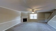 This two-story home offers a well-appointed layout with classic design elements throughout. The main living area is a standout feature, showcasing a tile-surround fireplace with a decorative white wood mantel that serves as a natural focal point. A large window allows natural light to fill the room, complementing the neutral, warm-toned walls and plush wall-to-wall carpeting underfoot. Crown molding and a chair rail add refined architectural character, while a ceiling fan provides both practical airflow and an understated decorative touch. The textured ceiling adds depth to the space. The overall ambiance of the living area is open and inviting, offering a comfortable and versatile setting. The two-floor layout provides a clear separation of living spaces, allowing for both shared and private areas throughout the home. Neutral finishes and traditional detailing create a cohesive, move-in-ready aesthetic that offers a solid foundation for personalization. The combination of classic architectural touches and functional design make this a warm and welcoming space suitable for a variety of lifestyles.