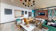 Located at 1500 Sherman Ave in Evanston, IL, this striking amenity floor showcases a bold mid-century modern aesthetic carried consistently throughout its interconnected spaces. The main lounge area features a statement Sputnik-style chandelier with brass and black globe accents, a warm cognac leather sofa, layered area rugs, and a large-format Scrabble board mounted as wall art — lending the space a playful yet sophisticated character. An adjacent sitting area offers floor-to-ceiling windows that flood the room with natural light and frame sweeping views of the Evanston skyline, complemented by a rich mahogany built-in bookcase wall and a brass multi-arm chandelier. The formal dining room is distinguished by dramatic teal botanical wallpaper, a coffered ceiling with a cascading gold chandelier, distressed hardwood flooring, and floor-to-ceiling windows opening to outdoor views. The kitchen features marble-look quartz countertops, a stainless gas cooktop, a textured white tile backsplash, and warm wood cabinetry with open display shelving. A generous interior corridor lined with floor-to-ceiling glass walls transitions seamlessly to a large outdoor terrace with a pergola structure and open-air seating, completing this thoughtfully designed, amenity-rich space.