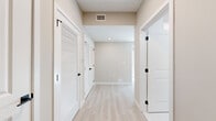 This well-appointed single-floor home offers three bedrooms and two bathrooms within a thoughtfully designed layout. Light-toned hardwood flooring flows consistently throughout the space, complementing the neutral warm-beige walls and crisp white trim that define the interior's clean, contemporary aesthetic.

The open-concept kitchen and living area serves as the heart of the home, featuring white shaker-style cabinetry, stainless steel appliances including a refrigerator, range, and microwave, and a light-colored countertop. Stylish pendant lights hang above the kitchen peninsula, adding a modern touch. Natural light pours in through large windows, offering scenic views of the surrounding neighborhood.

The spacious primary bedroom is generously sized, boasting oversized windows on two walls that flood the room with natural light and frame picturesque outdoor views. Its en-suite bathroom features marble-look tile flooring and walls, a walk-in shower, and access to a dedicated walk-in closet. The second bathroom is finished with the same marble-look tile and includes a single vanity with a white countertop and a framed mirror.

The additional bedrooms are bright and well-proportioned, each with ample natural light. A central hallway connects the rooms efficiently, with louvered closet doors providing convenient storage. The overall ambiance is modern, clean, and move-in ready.