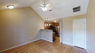 This single-floor residence offers a thoughtfully designed open-concept layout that seamlessly connects the living and kitchen areas. The space immediately impresses with its vaulted ceilings, which lend a sense of generous volume and airiness to the main living area. A ceiling fan with integrated lighting is centrally positioned, providing both comfort and illumination.

The kitchen is defined by warm honey-toned wood cabinetry paired with stainless steel appliances, including a refrigerator and built-in microwave. A peninsula counter serves as a natural divider between the kitchen and living space, offering additional prep area and casual seating potential. Pendant lights hang elegantly above the peninsula, adding a stylish focal point to the kitchen zone.

Light hardwood flooring runs throughout the main living area, contributing to a bright, cohesive aesthetic that complements the neutral beige wall tones. White trim and baseboards provide clean, classic contrast against the warm palette. A doorway visible from the main living area suggests additional rooms beyond, offering practical flow throughout the floor plan. Overall, the space strikes a balance between functional design and comfortable living, with architectural details that elevate the everyday experience.