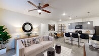 This single-story home in Denham Springs, Louisiana, offers a thoughtfully designed open-concept layout across three bedrooms and two bathrooms. The main living area seamlessly connects the living room, dining space, and kitchen, creating a cohesive and functional environment. Polished concrete floors flow throughout, lending the home a clean, contemporary aesthetic.

The living room features a ceiling fan, recessed lighting, and a glass-paneled door that introduces natural light. A rustic wood console table and round mirror accent the space. The kitchen is a standout feature, centered around a large granite-topped island with bar seating for multiple guests. Gray cabinetry, a white subway tile backsplash, pendant lighting, and black appliances—including a refrigerator, range, and over-the-range microwave—complete the well-appointed space.

The bedrooms are comfortably sized, with one featuring a ceiling fan and large windows dressed with curtain panels. The two bathrooms echo the home's modern palette, each showcasing granite-topped vanities with gray cabinetry. One bathroom includes a tub-shower combination with tiled surround and built-in shelving. The overall ambiance is bright, neutral, and move-in ready.
