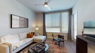 This single-story residence offers a thoughtfully designed layout that balances open communal spaces with private retreats. The living room serves as the heart of the home, featuring large windows with horizontal blinds and floor-length drape panels that invite an abundance of natural light. A ceiling fan overhead and warm-toned hardwood-style flooring add comfort and continuity to the space.

The kitchen is outfitted with stainless steel appliances, including a French door refrigerator, electric range, and built-in microwave. Light wood cabinetry pairs with granite countertops and a subway tile backsplash, while a center island with pendant lighting above provides additional prep space and casual seating. The kitchen opens naturally toward a dining area, enhancing the overall flow.

The bedroom offers a calm, restful atmosphere with plush carpeting, a ceiling fan, and a large window that fills the room with soft, diffused light. Neutral wall tones and understated décor contribute to a serene ambiance.

The bathroom is finished with light wood-tone cabinetry, granite countertops, a wide vanity mirror, and a shower-tub combination. Hardwood-style flooring extends throughout, maintaining a cohesive aesthetic across the space.