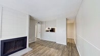 This single-floor residence offers a practical and comfortable layout across a thoughtfully arranged floor plan. The living area serves as the heart of the home, highlighted by a classic fireplace with a shiplap-style surround and durable wood-look flooring that extends throughout the common areas, lending a warm, cohesive aesthetic. A pass-through opening connects the living space to the kitchen, creating an open and communicative flow between rooms. The kitchen is well-appointed with white cabinetry, light countertops, a full suite of appliances including a black refrigerator and electric range, and a bright overhead fluorescent light. A dedicated entrance welcomes residents into the space, while two closets provide ample storage throughout. The generously sized bedroom is carpeted for comfort, features a ceiling fan with an integrated light fixture, a window that invites natural light, and direct access to a walk-in closet with built-in shelving. The neutral gray tones on the walls throughout the residence create a clean, move-in ready atmosphere, complemented by consistent white trim and baseboards that tie each room together with a polished finish.
