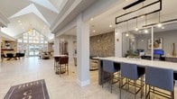 803 Corday is a thoughtfully designed community amenity space that seamlessly blends modern elegance with functional comfort across a single, expansive floor. The welcoming lobby greets visitors with a striking herringbone-patterned feature wall bearing the property's bold gold signage, complemented by tufted leather banquette seating and marble-topped tables. Light tile flooring flows throughout the main areas, reinforcing a bright, cohesive aesthetic. The grand lounge is a standout, boasting soaring vaulted ceilings, floor-to-ceiling windows that invite abundant natural light, and a rustic stone fireplace as a central focal point. A gold geometric chandelier adds a refined touch, while a billiards table and shuffleboard provide recreational options. A relaxed seating area with plush sofas and a wall-mounted television offers a comfortable retreat. The well-appointed coffee bar features sleek cabinetry, quartz countertops, and pendant lighting, conveniently positioned adjacent to a glass-enclosed business center equipped with workstations and printing resources. A quiet lounge nook with large windows and a smaller media room with curated décor and a television round out the space, offering residents a variety of settings for work, leisure, and socializing.