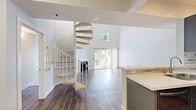 Located in the Westchester neighborhood of Los Angeles, this two-story, 2-bedroom, 3-bathroom home offers a thoughtfully designed layout across two floors. The main level is the larger of the two and showcases an open-concept living area with soaring double-height ceilings that amplify the sense of space and light. A corner fireplace with a classic white surround anchors the living room, while sliding glass doors and a clerestory window flood the space with natural light and provide views of lush greenery. Rich wood-look flooring runs throughout the main level, complementing the contemporary aesthetic. The kitchen is well-appointed with dark cabinetry, a mosaic tile backsplash, stainless steel appliances including a gas range, microwave, and refrigerator, and a peninsula with a quartz countertop offering additional prep and seating space. A striking spiral staircase leads to the upper level, where the bedrooms are finished with plush carpeting and neutral tones. The primary bedroom includes a mirrored sliding-door closet, while a dedicated walk-in closet with built-in shelving provides additional storage. Three bathrooms feature clean, modern finishes with wood-toned vanities and tile surrounds. The overall ambiance is bright, airy, and move-in ready.