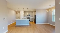 This well-appointed single-floor unit offers a clean, contemporary design throughout. The open-concept kitchen serves as the heart of the space, featuring gray shaker-style cabinetry, white quartz countertops, a white subway tile backsplash, and a full suite of stainless steel appliances including a gas range, built-in microwave, refrigerator, and dishwasher. A central island with an undermount sink and pendant lighting above adds both functionality and style. Light-toned hardwood flooring runs consistently throughout the unit, complementing the soft gray and taupe wall palette. A wide hallway connects the kitchen to the remaining rooms, with a convenient closet nearby. The bedrooms are generously sized, each featuring ceiling fans and multiple windows that invite abundant natural light. One bedroom opens directly to an outdoor balcony through glass French doors, offering views of the surrounding neighborhood. The bathroom is finished with a gray floating vanity, white quartz countertop, a large mirror, and stylish vanity lighting. Recessed lighting and clean white trim throughout the unit contribute to a bright, polished aesthetic. The overall design is cohesive and modern, creating a comfortable and functional living environment.