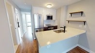 This thoughtfully updated single-floor residence showcases a cohesive modern design with warm hardwood flooring that runs continuously throughout the living spaces. The open-concept kitchen serves as a central feature, equipped with white shaker-style upper cabinets, dark lower cabinetry, and a classic white subway tile backsplash. A peninsula with a quartz countertop and a matte black faucet over a stainless steel sink provides additional prep space and informal seating. Stainless steel appliances, including a full-size refrigerator, microwave, and range, complete the well-appointed kitchen, while rustic wood floating shelves add a warm, decorative touch. The living and bedroom areas benefit from expansive floor-to-ceiling windows framed in sleek black, inviting abundant natural light and offering open urban views of the surrounding cityscape. A private balcony is accessible directly from the living area. Ceiling fans in the bedrooms add both comfort and style. The bathroom features large-format subway tile surrounding a full soaking tub and shower combination, complemented by a quartz vanity top, wood cabinetry, chrome fixtures, and an illuminated medicine cabinet mirror. Neutral tones and clean lines throughout create a bright, cohesive, and move-in-ready environment.