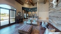 Located in Richmond, TX, this single-story community clubhouse on Meadow Ranch Pkwy delivers a refined rustic-modern aesthetic throughout its open, expansive interior. The space is defined by soaring ceilings accented with exposed wood beams and wood-paneled inlays, creating a warm yet dramatic architectural character that sets the tone from entry to exit.

The main lounge area features a striking reclaimed wood accent wall adorned with a longhorn skull mount, paired with a richly tufted leather sofa, upholstered accent chairs with teal cushions, and a geometric parquet-style wood floor that anchors the entire space. Decorative area rugs and layered lighting, including recessed fixtures and pendant lights, contribute to an inviting atmosphere.

A kitchenette bar area showcases a stone-clad base topped with light granite countertops, industrial-style pendant lighting, white cabinetry, subway tile backsplash, and bar seating — ideal for resident gatherings and events.

The dining area benefits from floor-to-ceiling black-framed glass doors that flood the space with natural light while offering views of the outdoor amenity area. Stone-textured accent walls and wainscoting throughout add additional layers of texture and sophistication, unifying the space's cohesive, upscale ranch-inspired design.