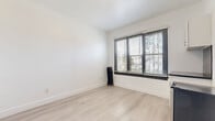 Located at 5849 Sunset Boulevard in the heart of Hollywood, Los Angeles, this efficiently designed studio unit offers a clean, modern aesthetic throughout. The open main living area features light-toned wood laminate flooring and bright white walls that enhance the sense of space, with a large window dressed in sleek black blinds allowing natural light to filter in and offering a view of the surrounding greenery.

The kitchenette is thoughtfully integrated into the living area and includes white shaker-style cabinetry, a dark stone countertop, and a striking black mosaic tile backsplash that serves as a stylish focal point. A stainless steel compact refrigerator completes the kitchen setup. Black-trimmed doorframes provide a bold contrast against the white walls, lending the unit a contemporary edge.

The bathroom is finished in an all-white palette with large-format tile flooring, a full soaking tub with shower, a vanity with mirror, and a towel bar — clean and functional in design. A dedicated closet offers practical storage. The unit's single-floor layout and cohesive design make it a streamlined and functional living space in one of Los Angeles' most iconic and vibrant neighborhoods.