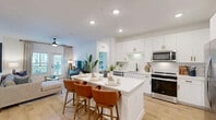 Located at 9500 Grandtree Ave in Venice, FL, this single-story 2-bedroom, 2-bathroom residence offers a thoughtfully designed open-concept layout that seamlessly connects the kitchen, dining, and living areas. The kitchen is a standout feature, showcasing crisp white shaker cabinetry with gold-toned hardware, a classic subway tile backsplash, stainless steel appliances, and a large center island with bar seating — ideal for casual dining and entertaining. Light wood-style flooring flows throughout the main living areas, enhancing the bright and airy ambiance created by recessed lighting and a ceiling fan overhead. The living room is filled with natural light from large windows that offer views of the outdoors. Both bedrooms are generously sized, carpeted for comfort, and feature ceiling fans and large windows. The primary bedroom is notably spacious, with ample natural light and direct access to its own bathroom, which includes a dual-sink vanity with gray cabinetry and gold hardware, and a walk-in closet. A second well-sized bedroom and full bathroom provide flexibility for guests or a home office. The dedicated laundry room houses a full-size washer and dryer with built-in shelving above. Two closets offer practical storage throughout the home.