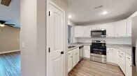 This two-story home offers a clean, modern interior with a cohesive design language carried throughout each level. The kitchen is a functional highlight, featuring white shaker-style cabinetry, granite countertops, a classic white subway tile backsplash, and a full suite of stainless steel appliances including an electric range, built-in microwave, and dishwasher. Light wood-tone luxury vinyl plank flooring runs through the kitchen and extends into the main hallway, lending warmth and continuity to the first floor.

The main hallway connects key living areas and leads to a spacious living room equipped with a ceiling fan and natural light provided by multiple windows. A carpeted staircase connects the two floors, with additional carpeted rooms found throughout, offering comfort underfoot in the bedrooms. Each bedroom includes a ceiling fan and window, allowing for natural light and ventilation.

The bathrooms are well-appointed, each featuring white cabinetry with dark hardware, granite-topped vanities, and a tub-shower combination. The neutral gray tones on the walls throughout the home create a calm, versatile backdrop, while white trim and paneled doors add a crisp, finished look to every room.