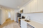 Located at 315 Anacostia Rd SE in Washington, DC, this single-floor, 3-bedroom, 1-bathroom home offers a clean and modern living environment with a thoughtfully organized layout. The open-concept kitchen, dining, and living area forms the heart of the home, featuring crisp white shaker-style cabinetry extending to the ceiling for ample storage, light quartz countertops, a single-basin sink, and a full suite of stainless steel appliances including a refrigerator, electric range, over-the-range microwave, and dishwasher. Recessed lighting brightens the space throughout. Light wood-tone flooring runs consistently across the main living areas and bedrooms, lending warmth and visual continuity to the interior. A central hallway connects the three bedrooms, each featuring white walls, natural light from windows with blinds, and closet storage. The primary bedroom offers its own dedicated closet space. The bathroom is finished with large-format marble-look wall tile surrounding a full soaking tub and shower combination, complemented by a white vanity and neutral tile flooring. Four closets and a pantry provide generous storage throughout. The overall aesthetic is bright, minimal, and move-in ready.