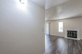This single-floor residence offers a practical and comfortable layout designed for everyday living. The living room serves as the heart of the home, showcasing rich, dark hardwood-style flooring, a textured popcorn ceiling, and a classic white brick fireplace with glass doors as a central focal point. Flanking the fireplace are two narrow vertical windows fitted with blinds, allowing natural light to filter into the space. A wall-mounted sconce light near the entryway adds an additional lighting element. A ceiling fan with integrated lighting is positioned in the adjoining dining area, which flows seamlessly into the kitchen via a pass-through counter. The galley-style kitchen is outfitted with white cabinetry, speckled laminate countertops, a stainless steel double-basin sink, a gas range with a ventilation hood, and a stainless steel refrigerator. A skylight overhead brightens the cooking space naturally. The bedroom features plush carpeting, neutral walls, and a textured ceiling, providing a quiet retreat. The bathroom is well-appointed with a combination tub and shower enclosed in a white surround, chrome grab bars for accessibility, a single-sink vanity with a speckled countertop, and hardwood-style flooring that carries throughout the wet areas.