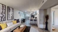This single-floor residence offers a thoughtfully designed open-concept layout that seamlessly connects the living, dining, and kitchen areas into one cohesive and functional space. Wood-look flooring flows throughout the main living areas, complemented by neutral-toned walls and a textured ceiling that adds subtle character.

The living room is bright and welcoming, featuring a window that allows natural light to filter in. It connects naturally to a dedicated dining area, which benefits from access to a private outdoor space through sliding glass doors fitted with vertical blinds.

The kitchen is a standout feature, showcasing granite countertops, dark cabinetry, and a peninsula with bar seating — ideal for casual dining or entertaining. A full suite of black appliances, including a refrigerator and range, is complemented by a tile backsplash and pendant lighting that adds a modern touch.

The bedroom is a comfortable retreat, finished with plush carpeting and a ceiling fan for year-round comfort. It includes access to a walk-in closet, providing ample storage. Windows allow natural light to brighten the space while maintaining a sense of privacy.

Overall, this residence combines practical design with contemporary finishes to create a cohesive and comfortable living environment.
