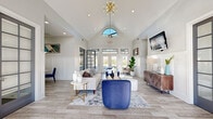 Located at 231 New Shackle Island Rd in Hendersonville, Tennessee, this single-floor community clubhouse offers a welcoming and well-appointed gathering space designed with both comfort and functionality in mind.

The entrance opens into a grand main lounge distinguished by dramatic vaulted ceilings that rise to a striking arched transom window, flooding the room with natural light. A gold sputnik chandelier serves as a focal point overhead, complementing the recessed lighting and a ceiling fan positioned near the entrance. Light wood-look tile flooring and crisp white wainscoting panels lend the space a clean, contemporary aesthetic. The lounge is furnished with a neutral sofa, a bold blue velvet accent chair, and layered area rugs, creating an inviting conversational arrangement. A wall-mounted television and a stylishly appointed sideboard anchor one end of the room, while French doors along the back wall open to exterior views, reinforcing the bright, airy atmosphere.

Adjacent to the main lounge, a dedicated dining and meeting room provides a more intimate setting. This space features plush carpet flooring, a solid wood dining table surrounded by upholstered blue chairs, a wall-mounted television set against a soft blue accent wall, and a ceiling fan. Natural light filters through shuttered windows, while decorative drapery and framed artwork add warmth to the room.