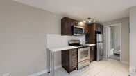 Located at 1150-1160 Rue Sherbrooke E in Montréal's vibrant Le Plateau-Mont-Royal area, this one-bedroom, one-bathroom unit is thoughtfully laid out across a single floor. The space is designed with a neutral, modern aesthetic that creates a bright and welcoming atmosphere throughout.

The kitchen is a functional highlight, featuring rich dark wood cabinetry, white subway tile backsplash, light stone countertops, and a full suite of stainless steel appliances including a gas range, built-in microwave, and refrigerator. Large white floor tiles reflect light and contribute to an open, airy feel in this area.

The bedroom offers a comfortable and private retreat, finished with light wood laminate flooring and warm beige walls that provide a calm, restful ambiance. A narrow vertical window allows for a touch of natural light. White baseboards and clean lines throughout maintain a cohesive, contemporary look.

The bathroom is well-appointed with grey textured floor tiles, a combined tub and shower enclosed by frosted glass, and dark wood vanity cabinetry that echoes the kitchen's design language. The hallway connects each space efficiently, ensuring a practical and logical flow throughout the unit. Overall, this unit presents a clean, move-in ready space with consistent finishes and a modern character.