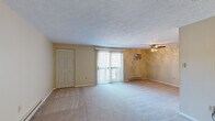 This single-floor unit offers a well-organized layout with distinct living, kitchen, and sleeping areas. The living room is generously sized, finished with neutral-toned carpet, textured ceilings, and a ceiling fan. A sliding glass door fitted with vertical blinds allows natural light to fill the space and provides outdoor access. A wall-mounted air conditioning unit and baseboard heaters ensure year-round climate control.

A pass-through opening connects the living room to the kitchen, creating an open, communicative flow between the two spaces. The kitchen is equipped with rich, dark cabinetry, granite-style countertops, and a full suite of stainless steel appliances, including a refrigerator, electric range, and dishwasher, complemented by wood-look flooring.

The bedrooms are carpeted and bright, each featuring baseboard heating and windows that bring in natural light. At least one bedroom includes a double-door closet with built-in wire shelving for organized storage. A compact half bathroom features a wall-mounted sink, toilet, wood-look flooring, and an oval mirror with overhead lighting, offering a clean and functional design throughout.