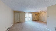 This single-floor unit offers a well-organized layout with distinct living, kitchen, and sleeping areas. The living room is generously sized, finished with neutral-toned carpet, textured ceilings, and a ceiling fan. A sliding glass door fitted with vertical blinds allows natural light to fill the space and provides outdoor access. A wall-mounted air conditioning unit and baseboard heaters ensure year-round climate control.

A pass-through opening connects the living room to the kitchen, creating an open, communicative flow between the two spaces. The kitchen is equipped with rich, dark cabinetry, granite-style countertops, and a full suite of stainless steel appliances, including a refrigerator, electric range, and dishwasher, complemented by wood-look flooring.

The bedrooms are carpeted and bright, each featuring baseboard heating and windows that bring in natural light. At least one bedroom includes a double-door closet with built-in wire shelving for organized storage. A compact half bathroom features a wall-mounted sink, toilet, wood-look flooring, and an oval mirror with overhead lighting, offering a clean and functional design throughout.