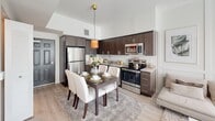 This single-floor unit presents a clean, contemporary design with a well-appointed open-concept layout connecting the kitchen and living area. The kitchen is outfitted with dark walnut-toned cabinetry, granite countertops, a white subway tile backsplash, and a full suite of stainless steel appliances including a range, over-the-range microwave, dishwasher, and refrigerator. Track lighting runs along the kitchen ceiling, providing focused task illumination throughout the space.

Light-toned hardwood flooring extends seamlessly from the kitchen through the living area, contributing to a bright, cohesive aesthetic. The living area benefits from abundant natural light through floor-to-ceiling sliding glass doors dressed with vertical blinds, with a ceiling fan overhead enhancing comfort. A secondary room, accessible via an open doorway, also features a window and ceiling fixture, offering versatility as a bedroom or flex space.

The bathroom is finished with large-format tile flooring and wall surrounds, a granite-topped vanity with dark wood cabinetry, an undermount sink, and a full soaking tub with a shower. Throughout the unit, the neutral white walls, consistent flooring, and modern fixtures combine to create a clean, move-in-ready living environment.