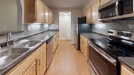 This single-floor residence offers a thoughtfully laid-out floor plan designed for comfortable everyday living. The galley-style kitchen is a functional highlight, featuring warm wood cabinetry, dark granite-style countertops, a subway tile backsplash, hardwood-style flooring, and a full suite of stainless steel appliances including a refrigerator, dishwasher, and built-in microwave — providing ample storage and prep space.

The living area is generously sized, finished with plush neutral carpeting and a ceiling fan, lending a warm and comfortable ambiance. Natural light filters in through multiple windows fitted with horizontal and vertical blinds throughout the home. The bedrooms are well-proportioned with soft carpeted floors, large windows with views of surrounding greenery, and dedicated closet space. One bedroom features a roomy walk-in closet with wire shelving and hanging rods, offering excellent organization potential. Another bedroom includes a standard reach-in closet.

The full bathroom is cleanly finished with large-format tile flooring, a wood-toned vanity with ample cabinet storage, and a tiled tub and shower combination outfitted with chrome fixtures. Overall, the space presents a clean, neutral palette throughout, creating a bright and move-in-ready environment.