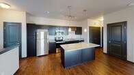 Located at Dodd Boulevard in Lakeville, Minnesota, this single-floor residence offers a well-designed open layout that seamlessly connects the kitchen, dining, and living areas. The kitchen is a standout feature, showcasing dark espresso cabinetry, granite countertops, a center island with pendant lighting, stainless steel appliances including a refrigerator, range, and microwave, a double-basin sink, and a distinctive built-in wine rack. Hardwood-style flooring flows throughout the main living spaces, complementing the contemporary aesthetic.

The living area is generously proportioned, bathed in natural light from multiple windows dressed with horizontal blinds. A ceiling fan provides year-round comfort, while an arched doorway adds an architectural detail that connects the living space to adjacent areas. Bedroom spaces feature plush carpeting, ceiling fans, and well-sized windows that allow ample daylight. The bathroom includes granite-topped vanity cabinetry, a combined tub and shower, and coordinating fixtures. The overall ambiance of the unit is clean, modern, and functional, with consistent finishes throughout that create a cohesive and inviting living environment.