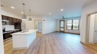 This well-appointed 2-bedroom, 2-bathroom residence in McCordsville, Indiana offers a thoughtfully designed single-floor layout with modern finishes throughout. The open-concept living and kitchen area serves as the heart of the home, featuring light wood-style flooring, recessed lighting, and a ceiling fan. The kitchen is a standout, showcasing rich dark cabinetry, white subway tile backsplash, stainless steel appliances including a refrigerator, range, and microwave, and a generously sized white-topped island with a built-in sink and stylish pendant lighting. The living area flows seamlessly toward a glazed door opening to an outdoor balcony, filling the space with natural light. Both bedrooms are carpeted and offer comfortable proportions, with the primary bedroom featuring its own balcony access and ceiling fan. Three closets, including walk-in closets with wire shelving systems, provide ample storage. The bathrooms are finished with clean white tile surrounds on the tub-shower combinations and light wood-style flooring. Two hallways connect the layout efficiently. The entry area is bright and welcoming, with recessed lighting and a clean, neutral palette carried throughout the entire residence.