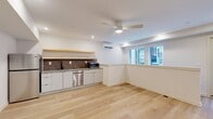 Located at 2009 North Howard Street in Philadelphia, PA, this two-floor unit offers a clean, modern aesthetic spread across two well-proportioned levels. Light oak hardwood flooring flows throughout both floors, creating a warm and cohesive atmosphere.

The lower floor houses the main living area and kitchen. The open-plan kitchen is outfitted with flat-front white cabinetry, stainless steel appliances including a refrigerator and dishwasher, a single-basin sink with a matte black faucet, and a textured stone tile backsplash. A natural wood floating shelf adds a warm accent above the countertop. A wall-mounted mini-split unit provides climate control, while recessed lighting and a ceiling fan with integrated light keep the space bright and comfortable. Windows along the wall allow natural light to filter in. A bathroom on this floor features neutral large-format tile flooring, a wall-mounted sink, and matte black hardware accents.

The upper floor serves as an open living room, offering a versatile, airy space with recessed lighting, a ceiling fan, a mini-split system, and crisp white walls. A modern staircase with sleek black metal railings connects the two floors, serving as a subtle architectural focal point. The overall design is minimal, clean, and move-in ready.