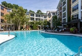 Located in Alpharetta, GA 30022, this residential community showcases thoughtfully designed outdoor amenities set within a multi-story brick and siding building complex. The centerpiece of the community is a generously sized resort-style swimming pool with crystal-clear turquoise water, surrounded by a stone paver deck outfitted with lounge chairs and seating areas ideal for relaxation. The pool area is secured by a decorative black wrought iron gate with brick columns, providing both privacy and visual appeal.

Adjacent to the pool, a covered outdoor kitchen and grilling station features a built-in brick surround, stainless steel grill, and an overhead pergola draped with hanging florals, creating an inviting space for outdoor entertaining. The grounds are extensively landscaped with mature trees, ornamental shrubs, colorful caladiums, hostas, and flowering plants that line meandering concrete walkways throughout the property. Lush greenery and well-maintained garden beds frame building entrances accented with French doors and private balconies. The overall ambiance reflects a carefully maintained, amenity-rich environment that balances community living with natural surroundings in a suburban Alpharetta setting.