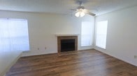 This single-story space in Arlington, Texas offers a welcoming living area defined by a combination of practical and classic design elements. The living room serves as the focal point of the space, anchoring around a brick-surround fireplace with a clean white mantle, providing both a functional heating source and a charming aesthetic centerpiece. Rich, dark hardwood flooring extends throughout the room, adding warmth and a sense of continuity to the space.

Natural light filters into the room through windows dressed with simple white blinds, brightening the neutral-toned walls and creating an open, airy feel. A ceiling fan with an integrated light fixture is centrally mounted, offering both illumination and efficient air circulation. The textured ceiling adds a layer of traditional character to the overall design.

The layout is straightforward and functional, with clean baseboards and uncluttered wall space that allow flexibility for furniture arrangement. The combination of the fireplace, hardwood floors, and natural light creates a comfortable and inviting atmosphere well-suited for everyday living.