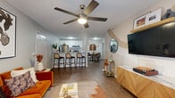 This thoughtfully designed single-floor residence offers a seamless open-concept layout that connects the living, dining, and kitchen areas into one cohesive, flowing space. The living room is a standout, featuring a ceiling fan, warm wood-look flooring, and large windows dressed in rich drapery that invite natural light. A distinctive curved, two-tone accent wall adds an artistic focal point, complementing the wall-mounted TV and stylish media console nearby.

The kitchen is well-appointed with white cabinetry, stainless steel appliances, and a peninsula with bar seating — ideal for casual dining or entertaining. A dedicated dining area sits just beyond, creating a natural transition between spaces.

The primary bedroom is generously sized with plush carpeting, a ceiling fan, a walk-in closet with built-in shelving, and a warm accent wall that adds depth and character. A second bedroom also features carpeting, a ceiling fan, a closet, and a dedicated desk area, making it versatile as a guest room or home office.

Two full bathrooms serve the residence, each finished with white cabinetry, light countertops, and wood-look flooring. One features a soaking tub with shower combination, while the other offers a separate shower. Together, the rooms create a cohesive, modern aesthetic with warm, eclectic design touches throughout.