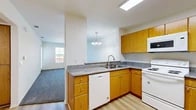 Located at 353 S Tustin St in Orange, CA, this single-floor, one-bedroom, one-bathroom unit offers a thoughtfully organized layout. The open-concept kitchen flows directly into the living room, creating a connected and functional living space. The kitchen is equipped with warm oak cabinetry, granite-style countertops, a built-in dishwasher, electric range, and overhead microwave, all set atop light wood-look flooring. A skylight and pendant chandelier provide ample illumination. The living room features plush carpet flooring and large windows that allow generous natural light and exterior views, along with access to a private entry door. The hallway entry is finished with light wood flooring and includes a closet for additional storage. The bedroom is a comfortable size, carpeted, and features a window with vertical blinds. It is accompanied by a spacious walk-in closet outfitted with built-in shelving rods on two walls for organized storage. The bathroom offers a wide walk-in shower with grab bars and a handheld showerhead, reflecting an accessible and practical design. Throughout the unit, neutral tones and clean finishes create a bright, welcoming ambiance.