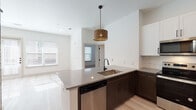 Located in Dallas's vibrant West Ninth Street corridor, this single-floor residence delivers a clean, contemporary aesthetic throughout. Light hardwood flooring runs continuously across the open layout, amplifying the natural light that pours in through multiple windows fitted with white blinds.

The kitchen serves as the centerpiece of the space, anchored by a peninsula island with a quartz countertop, undermount sink, and a statement woven pendant light overhead. Two-tone cabinetry — dark espresso lower cabinets paired with crisp white upper cabinets — frames a full suite of stainless steel appliances, including a refrigerator, electric range, over-the-range microwave, and dishwasher. A marble-style tile backsplash adds a refined finishing touch.

The open living area is bright and generously proportioned, with direct access to the exterior through a glass-panel door flanked by large windows, bathing the room in natural light throughout the day.

The bathroom is thoughtfully appointed with dark hardware accents, a bold chevron-patterned feature wall, a wood-toned vanity with a light countertop, and a glass-enclosed walk-in shower with large-format marble tile. An adjacent walk-in closet provides ample storage. A stacked Whirlpool washer and dryer unit rounds out the home's practical amenities.